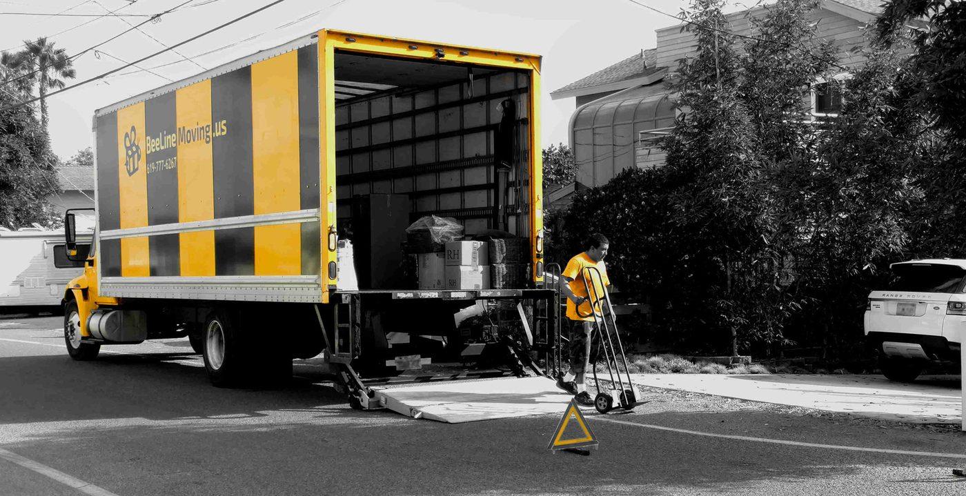The Beeline Moving yellow and black striped truck with its lift gate down and a crew member with a dolly